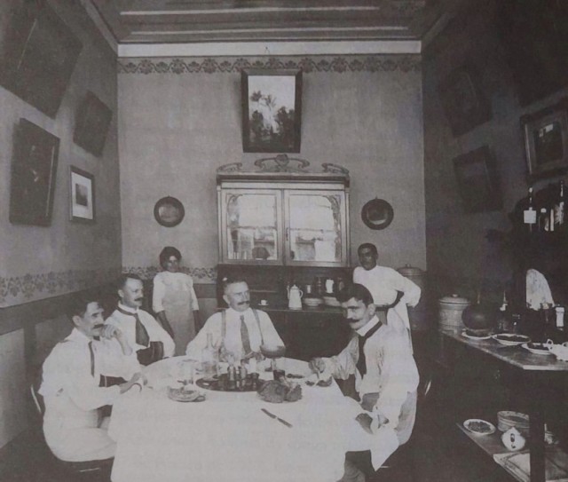 Foto em preto e branco de pessoas sentadas ao redor de uma mesa

Descrição gerada automaticamente