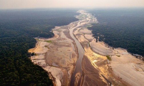 Vista aérea de rio amazônico durante a seca, com o leito quase totalmente exposto entre a floresta
